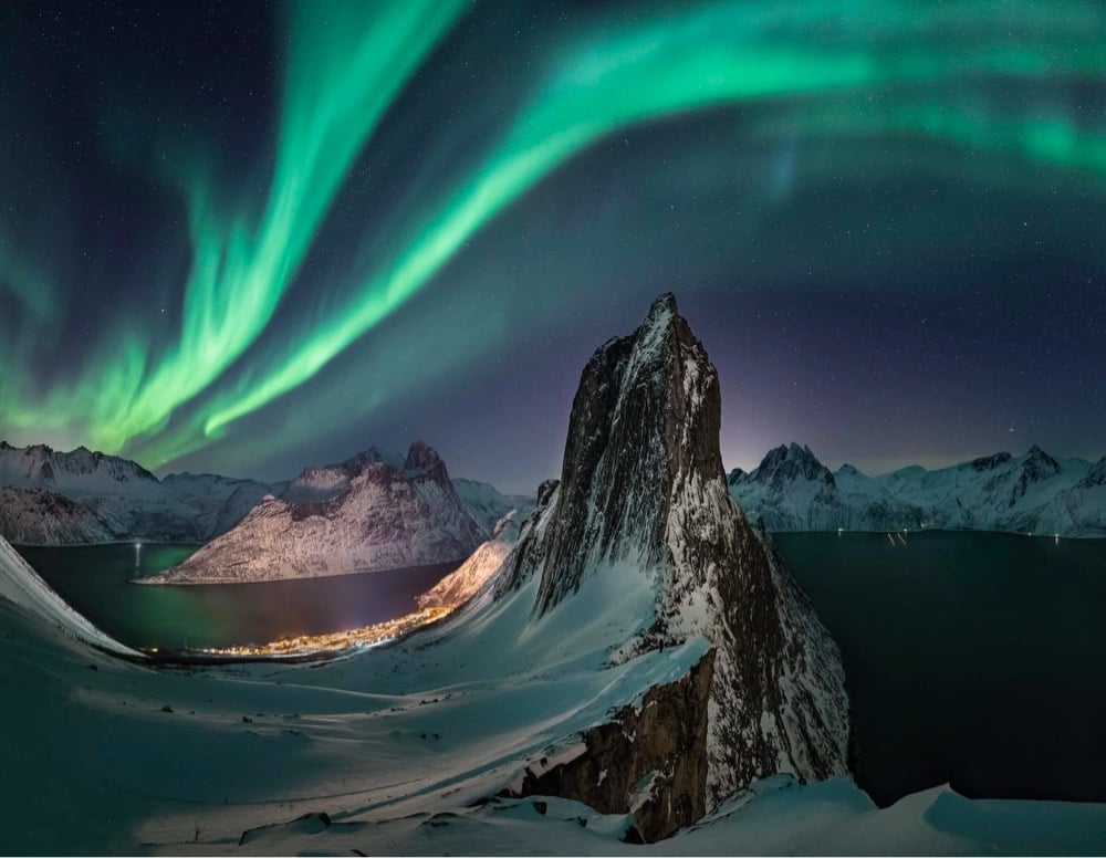 green aurora flows over a steep mountain peak