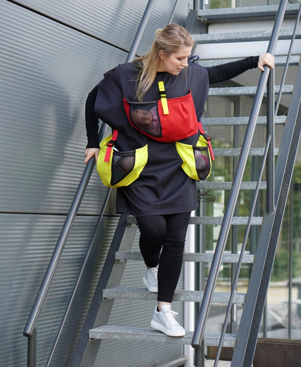 a woman wearing a baby evacuation apron with three fake babies in it going down some fire escape stairs