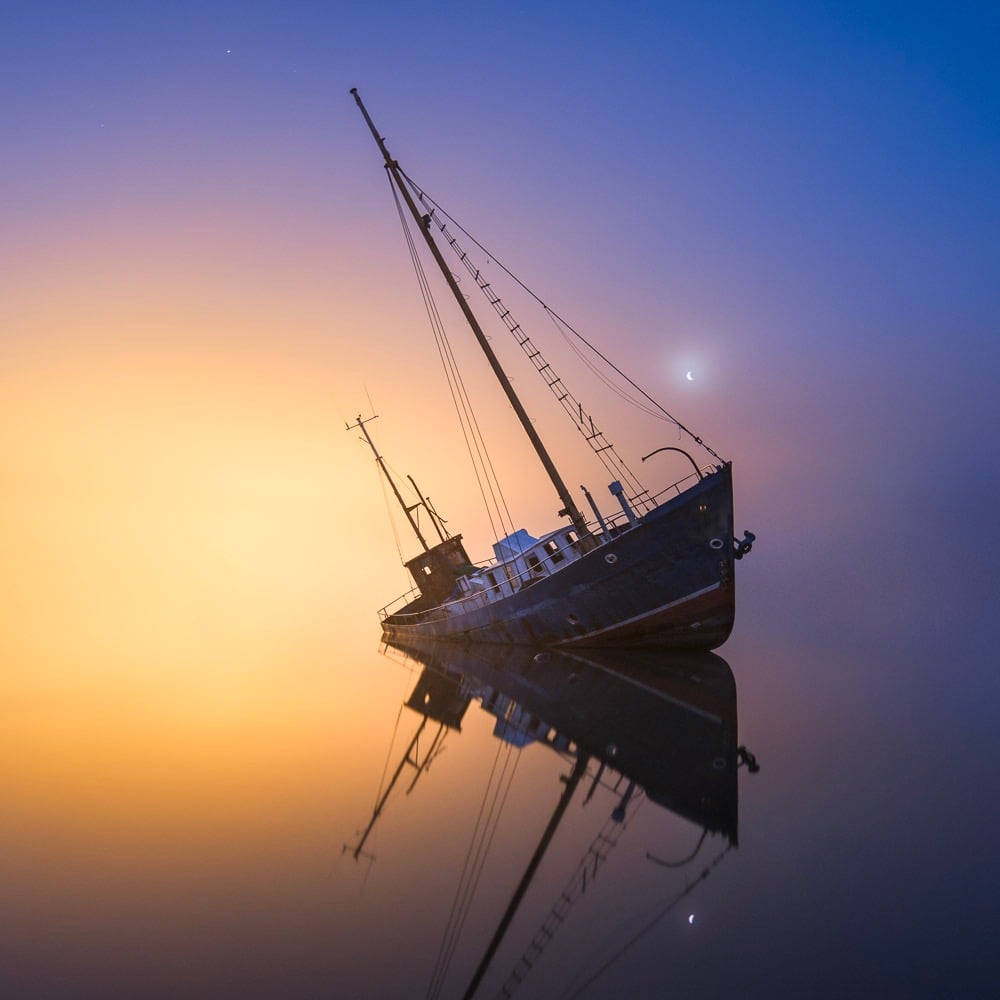 partially sunked boat under a colorful night sky