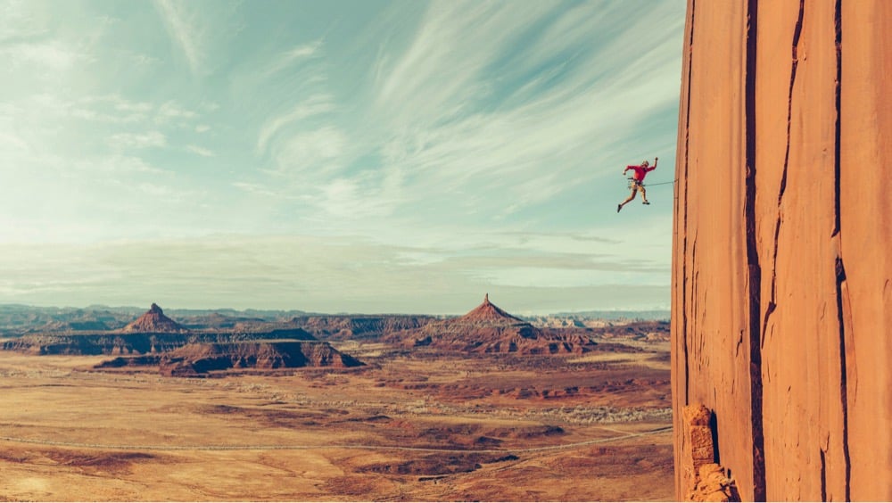 a climber jumps away from a cliff face