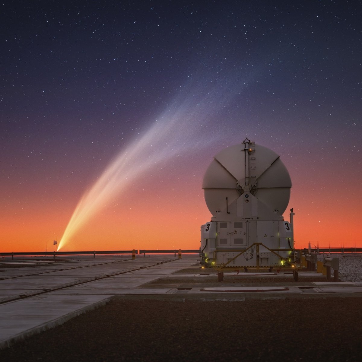 the long tail of a comet stretches over an observatory just after sunset