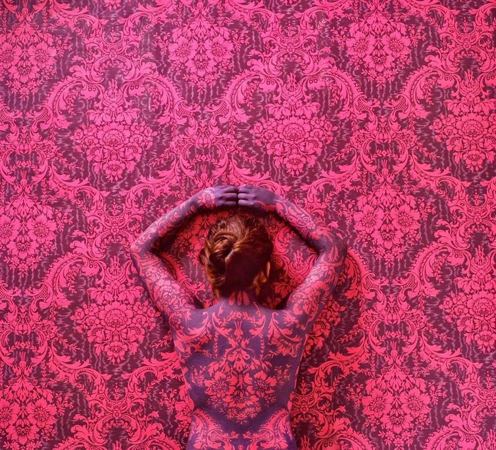 a woman camouflaged to blend into a patterned wall