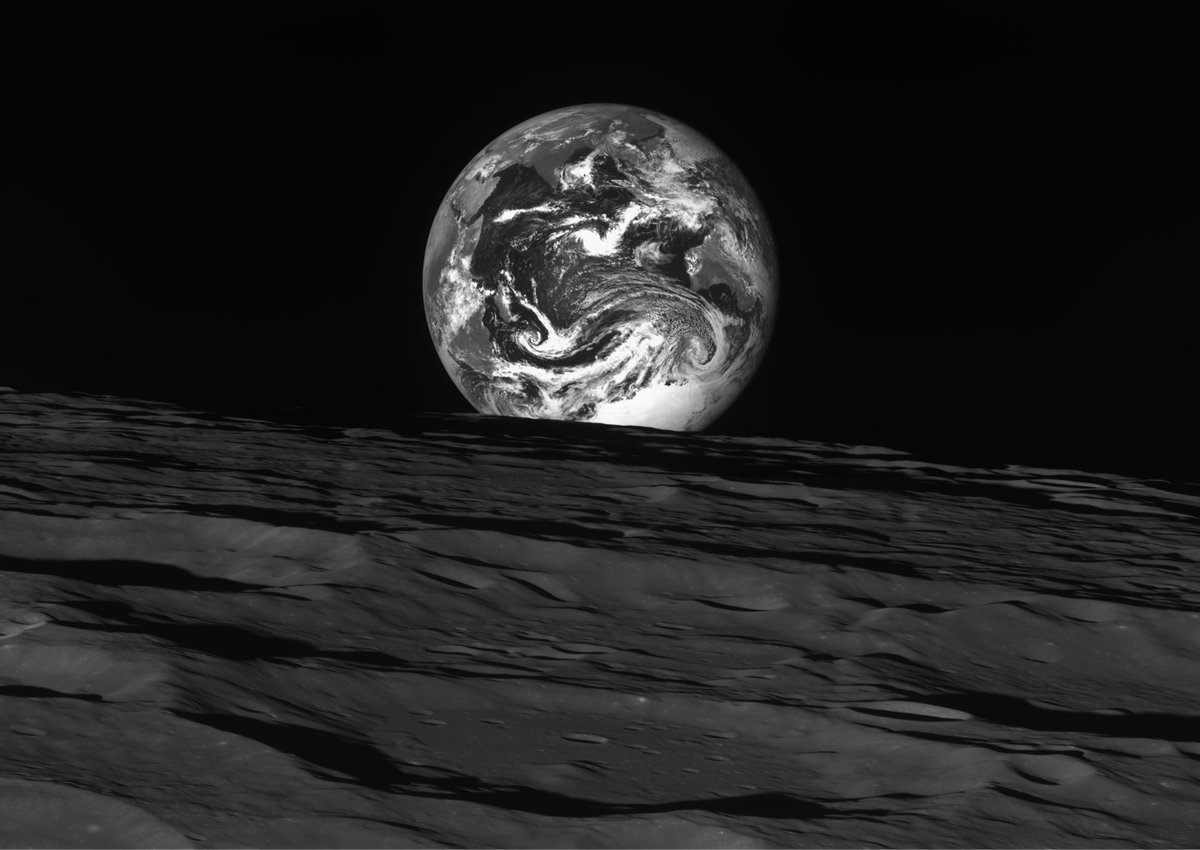 black and white photo of the Earth rising over the surface of the Moon