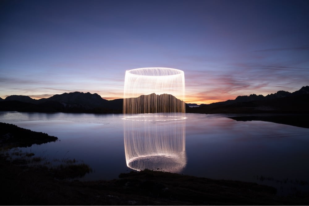 a bright cylinder of light over a dark lake surrounded by mountains