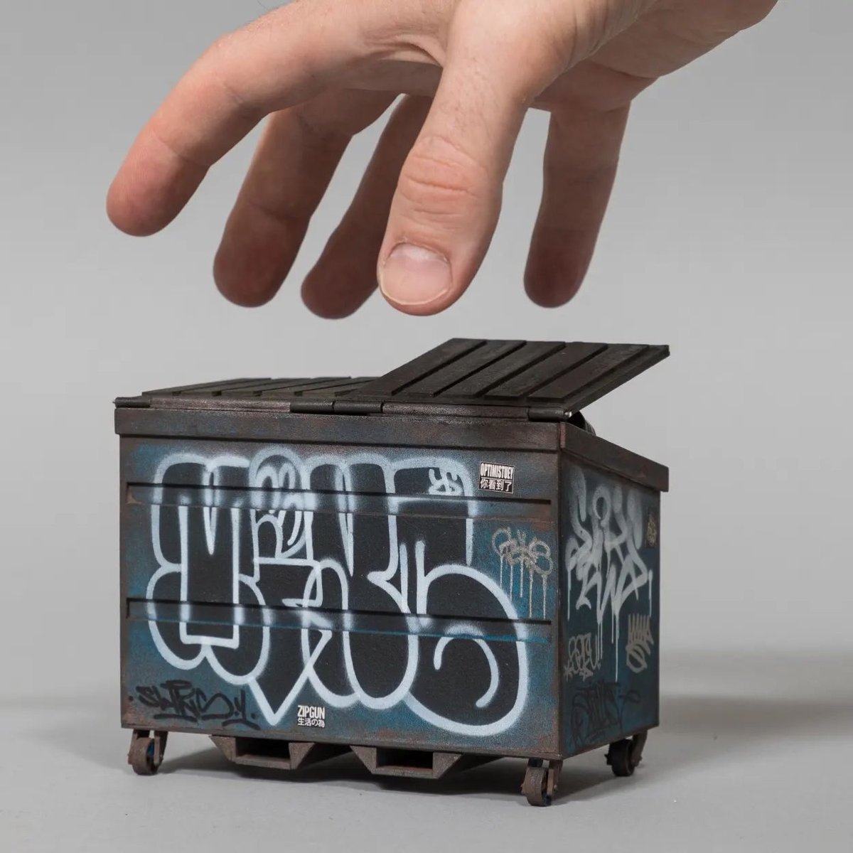 a miniature of a dumpster with a hand reaching down to grab it