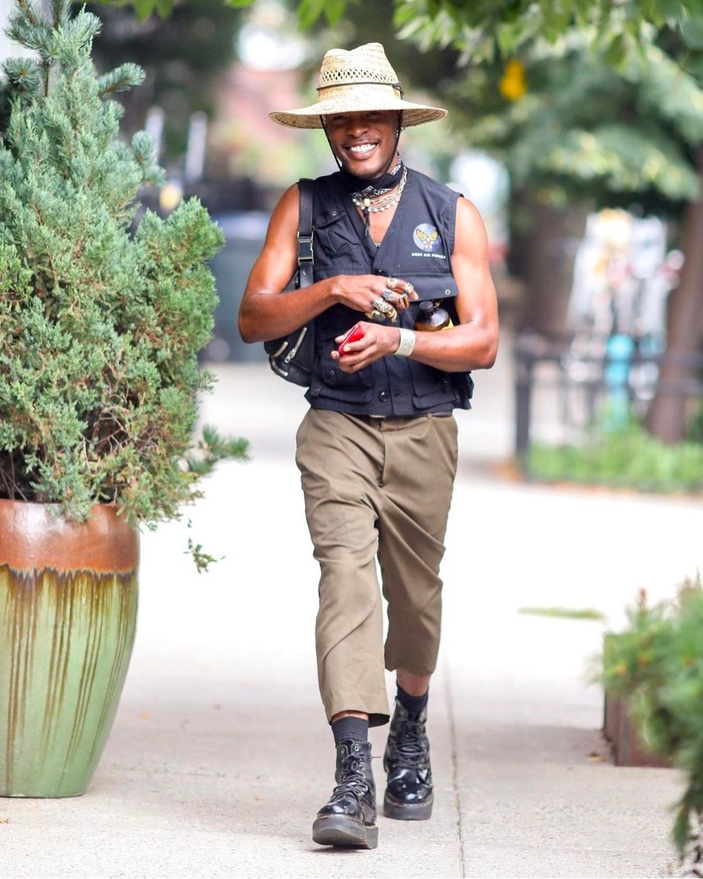 a man dressed in a wide brimmed hat, vest, and black boots walks down the street