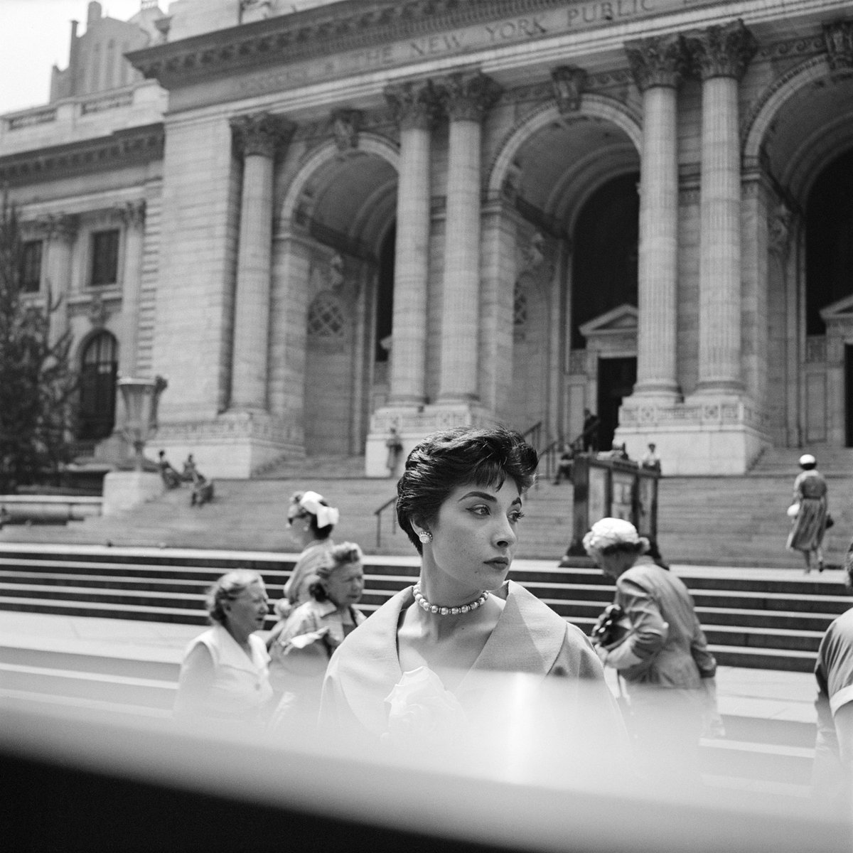 black & white photo of a woman looking to the right in front of a building